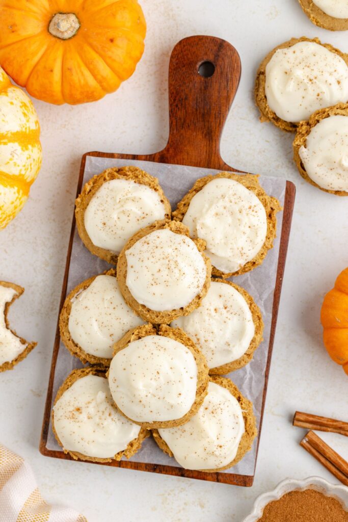 Pile of cream cheese frosted pumpkin cookies on a wooden board.