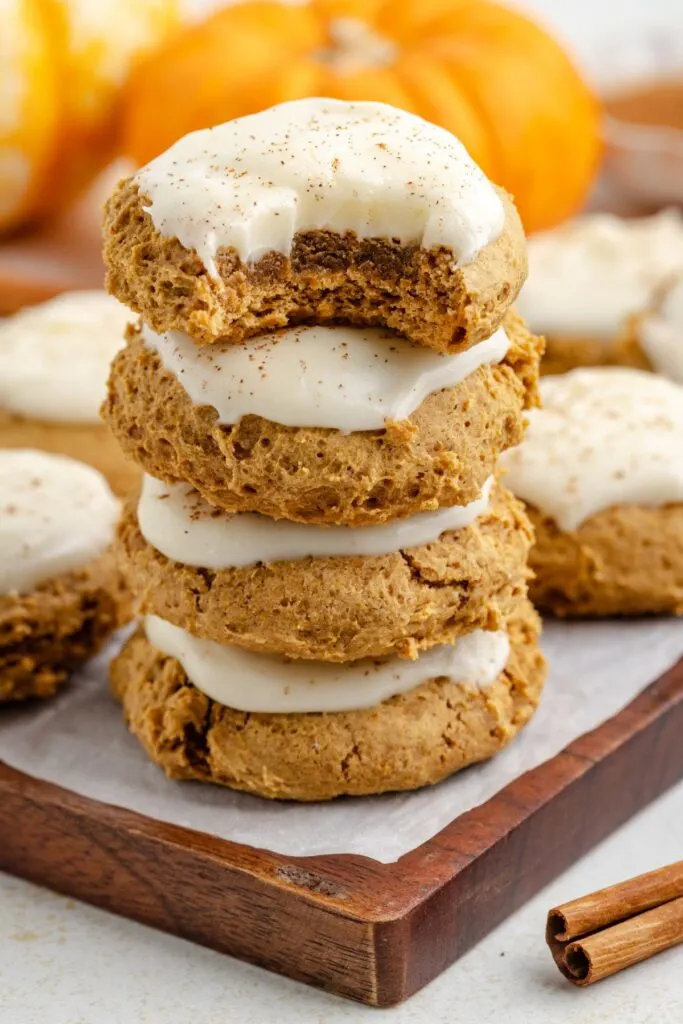 Stack of four cake mix pumpkin cookies with cream cheese frosting with a bite missing from the topped cookie.