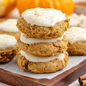 Stack of three frosted pumpkin cookies with cream cheese frosting.