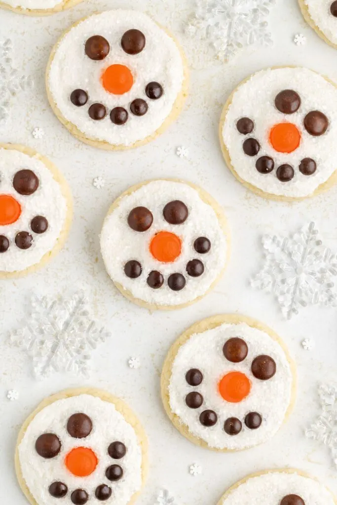 Snowman face cookies arranged on the counter surrounded by snowflakes.