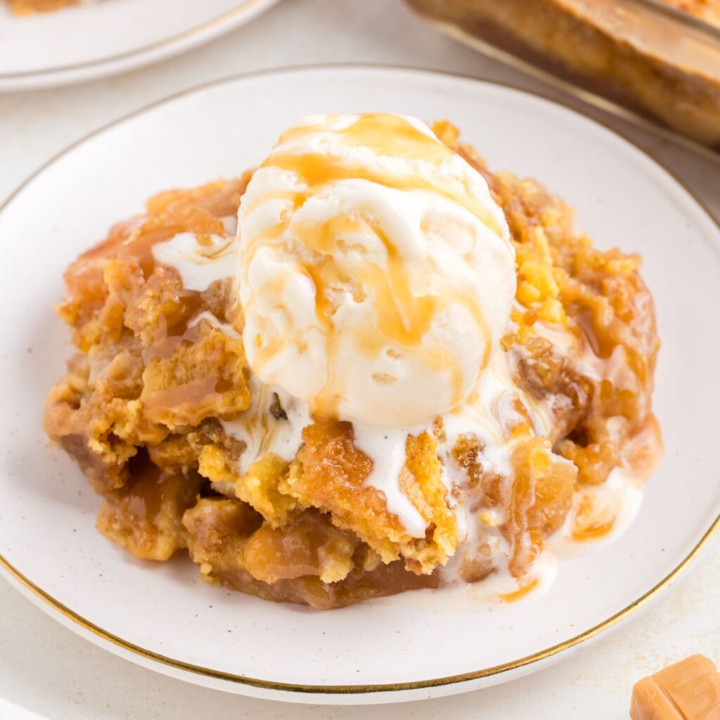 Caramel apple dump cake topped with vanilla ice cream and caramel sauce.