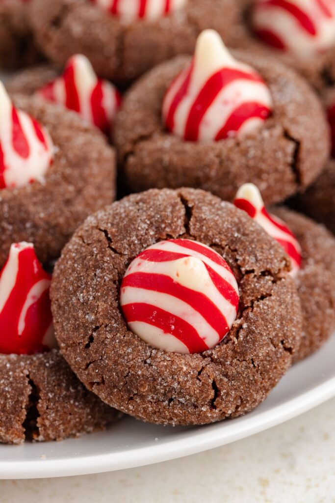 A plate of chocolate cookies topped with striped red and white peppermint kisses. The cookies are sprinkled with sugar, giving them a festive appearance.