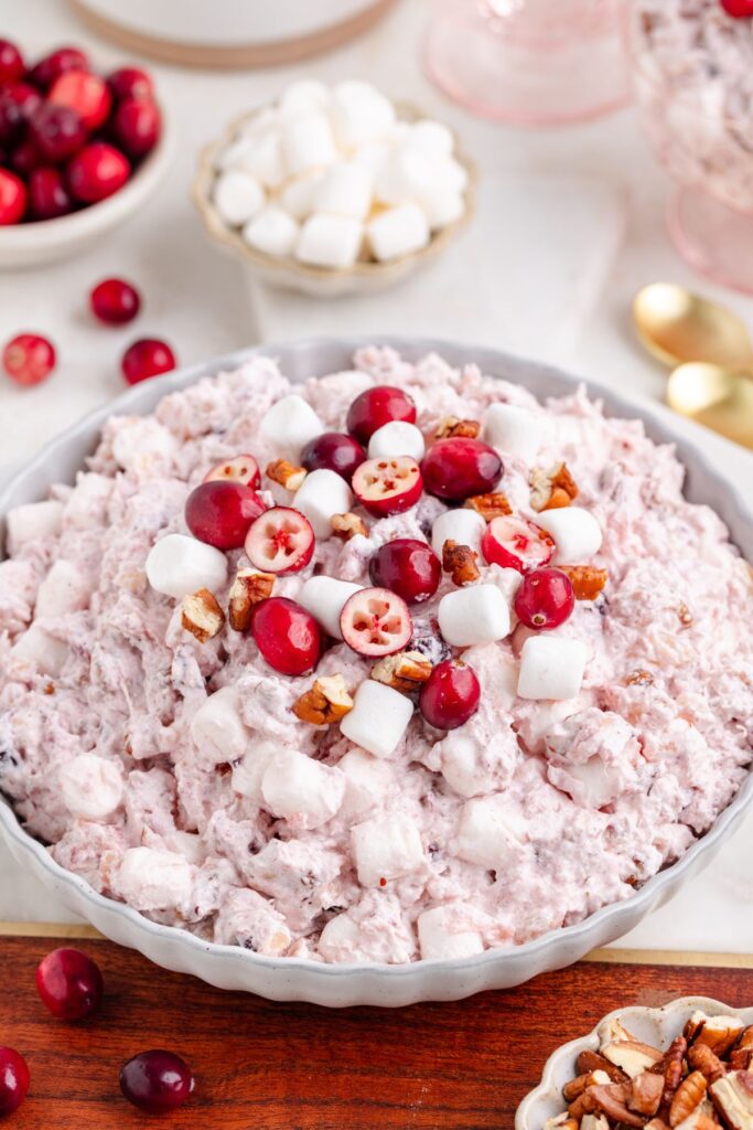 A bowl of creamy cranberry fluff salad topped with marshmallows, pecans, and sliced cranberries. 