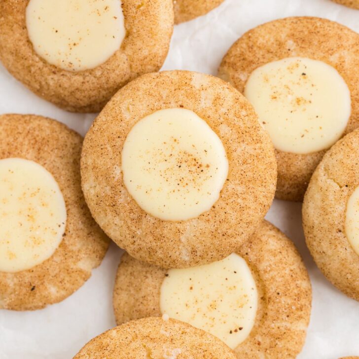 Close-up of several cinnamon cookies with creamy white centers, sprinkled with a touch of cinnamon on top, arranged on a white background.