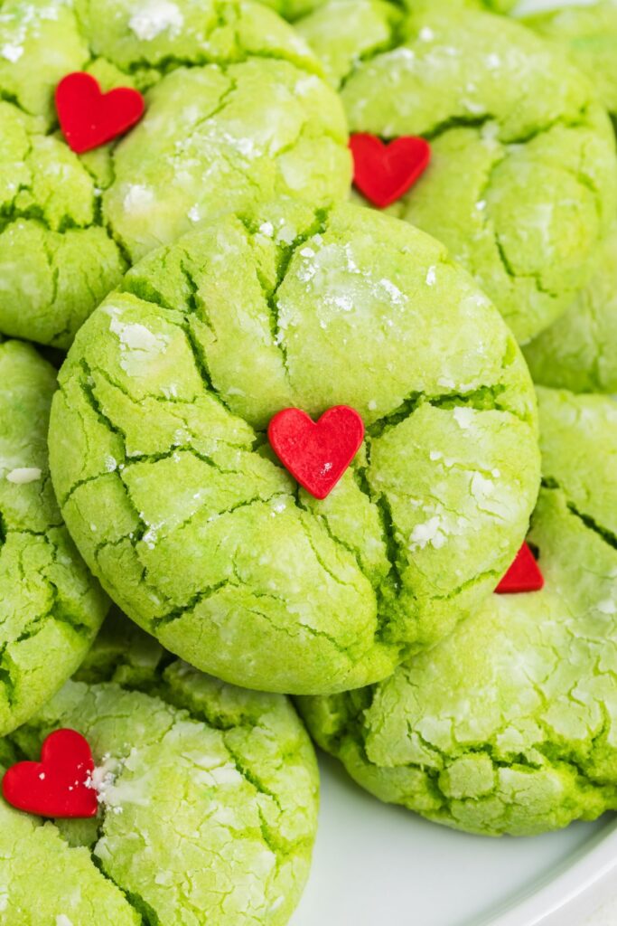 Pile of green Grinch crinkle cookies with red heart sprinkles.