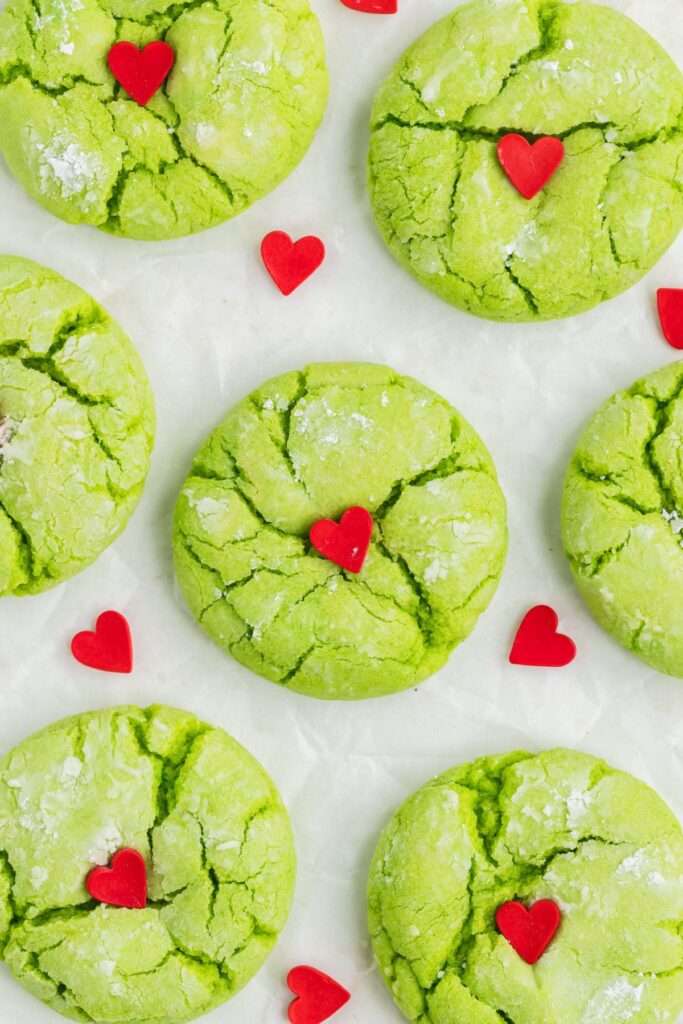 Green cake mix Grinch cookies with red hearts arranged on the counter.