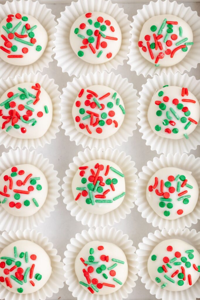 Rows of sugar cookie truffles in paper cups, each topped with red and green sprinkles.