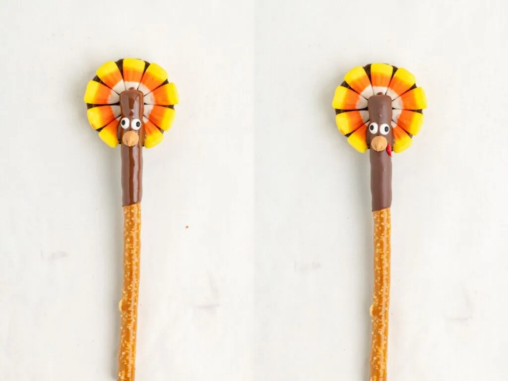 Two pretzel sticks each have a fun, edible turkey decoration on top. The turkeys are made with candy corn for feathers, chocolate for the body, and small candy eyes. They are placed side by side on a light background.