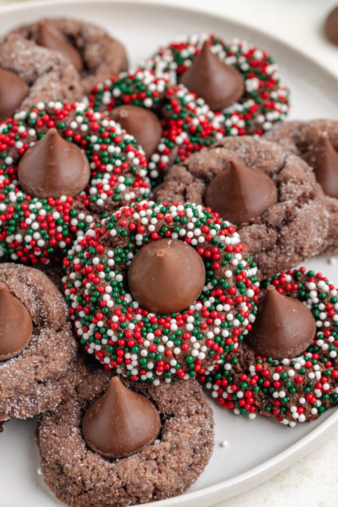 A plate of Chocolate Kiss Cookies, each one topped with chocolate kisses and adorned with red, green, and white sprinkles around the edges.