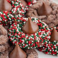 Close-up of chocolate cookies topped with a chocolate kiss, surrounded by festive red, white, and green sprinkles.