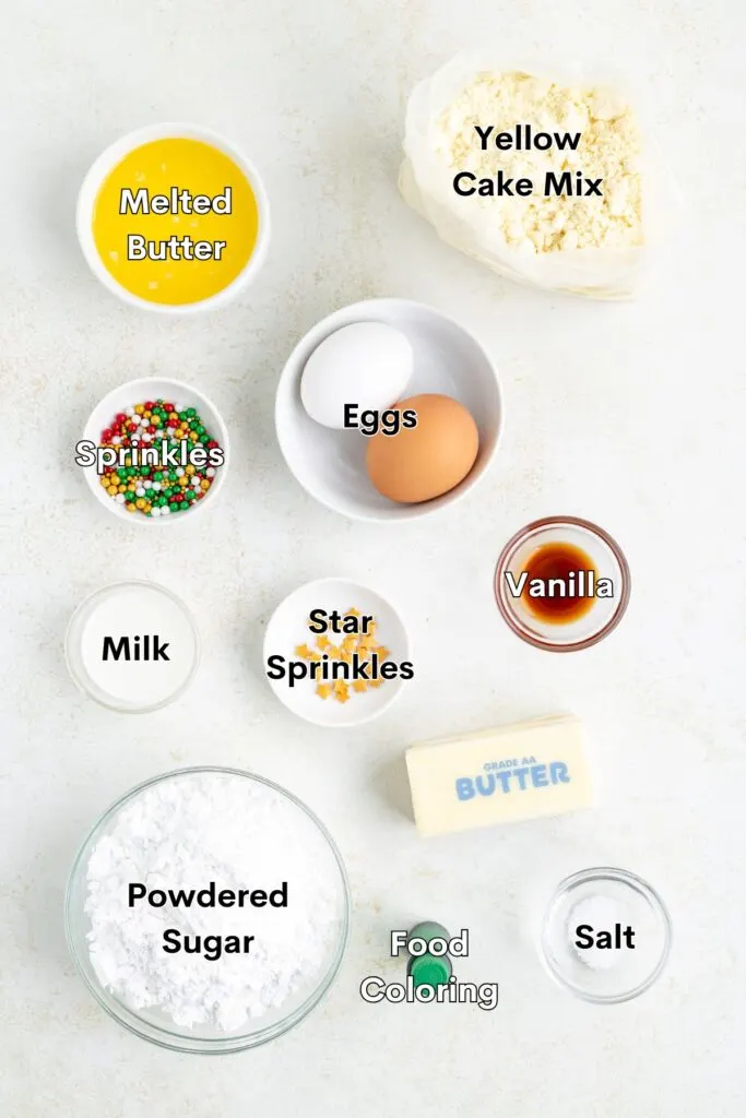 Containers of ingredients arranged on a light surface, including melted butter, yellow cake mix, two eggs, vanilla, sprinkles, star sprinkles, milk, powdered sugar, a stick of butter, food coloring, and a pinch of salt.