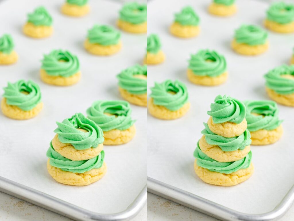 A baking tray with yellow cookies topped with swirls of green frosting, arranged in rows. On the right, three cookies are stacked in a tower. The cookies rest on parchment paper.