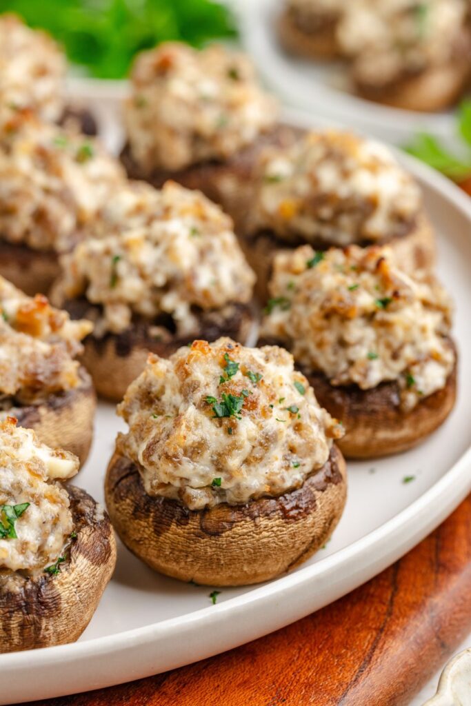 A plate of 3 Ingredient Sausage Stuffed Mushrooms topped with cream cheese and sausage, garnished with parsley. The mushrooms are arranged neatly on a white plate.