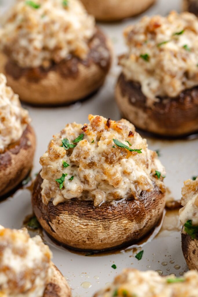 Close-up of 3 ingredient sausage stuffed mushrooms, topped with a creamy cheese mixture and garnished with fresh parsley. The mushrooms are baked to a golden brown, achieving a slightly crispy texture.