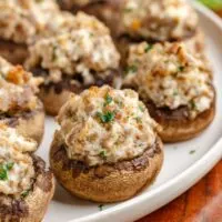 Plate of 3 Ingredient Sausage Stuffed Mushrooms garnished with chopped parsley, featuring a creamy, seasoned filling on a wooden table.