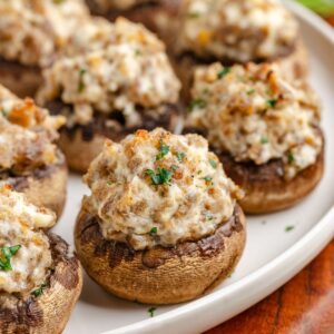 Plate of 3 Ingredient Sausage Stuffed Mushrooms garnished with chopped parsley, featuring a creamy, seasoned filling on a wooden table.