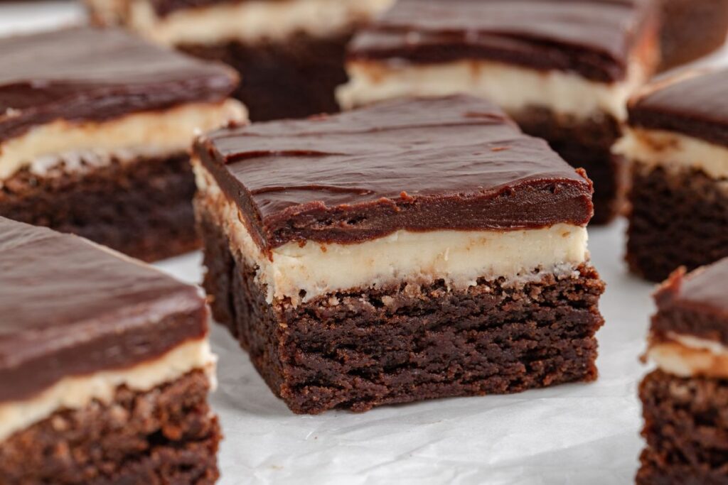 Close-up of Baileys Irish Cream brownies on white parchment paper. Each bar features a rich, dark chocolate base, a creamy Baileys-infused middle layer, and a smooth chocolate ganache topping.