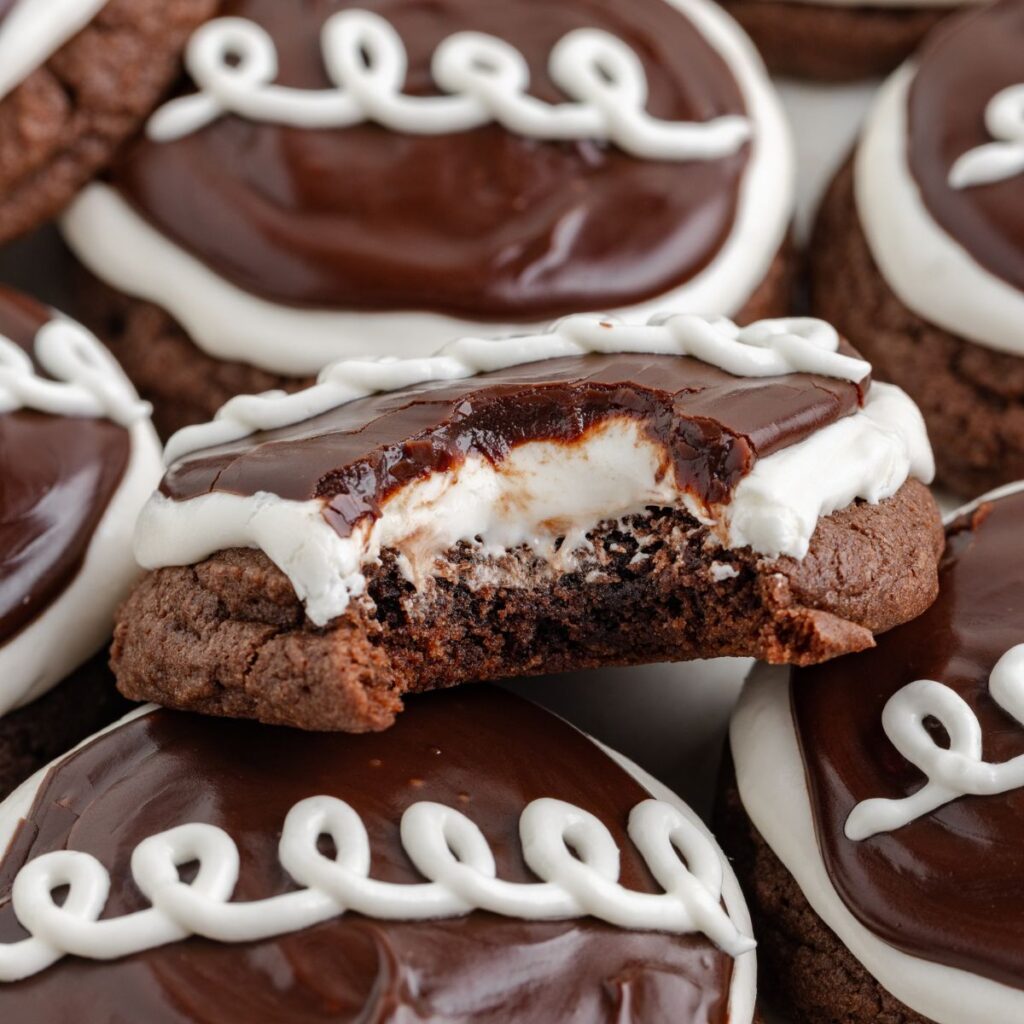 Hostess cupcake cookies: Chocolate cookies topped with glossy chocolate glaze and white icing swirls. One cookie has a bite taken out, revealing a creamy white filling.