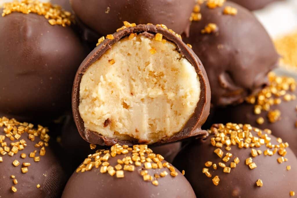 Close-up of Baileys truffles stacked with one truffle cross-sectioned in the center, revealing a creamy filling. The truffles are garnished with small golden sprinkles.