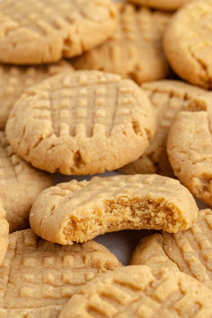 Close-up of several cake mix peanut butter cookies with a visible crisscross pattern. One cookie in the foreground has a bite taken out of it, revealing a soft interior. 