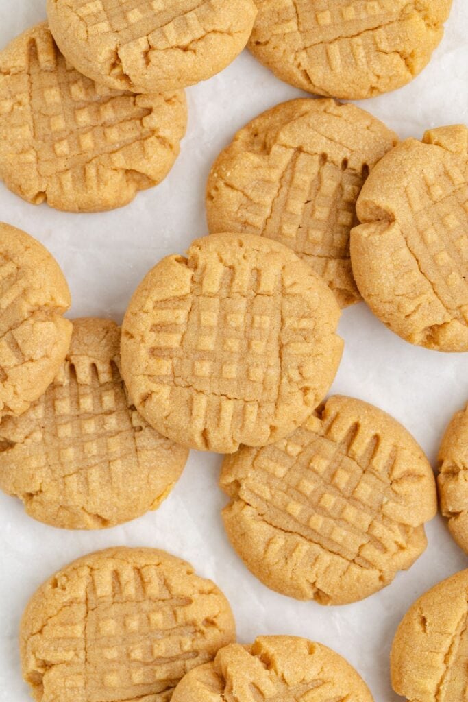 A collection of peanut butter cookies with a crisscross pattern on top, arranged on parchment paper. 