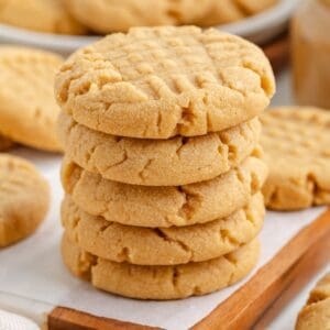 A stack of five cake mix peanut butter cookies with classic crisscross fork marks, resting on a piece of parchment paper on a wooden board.