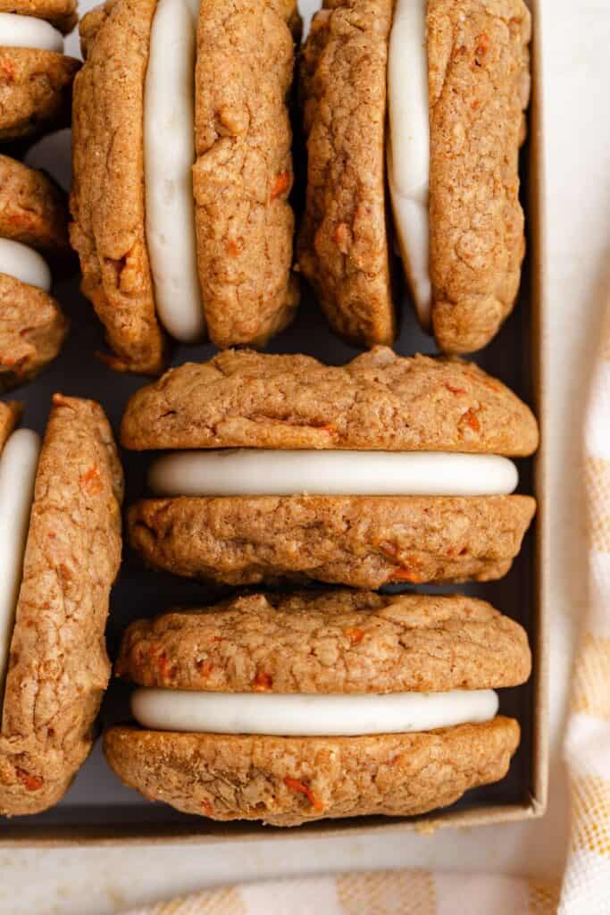 Tray of carrot cake cookies with cream cheese filling stacked side by side.