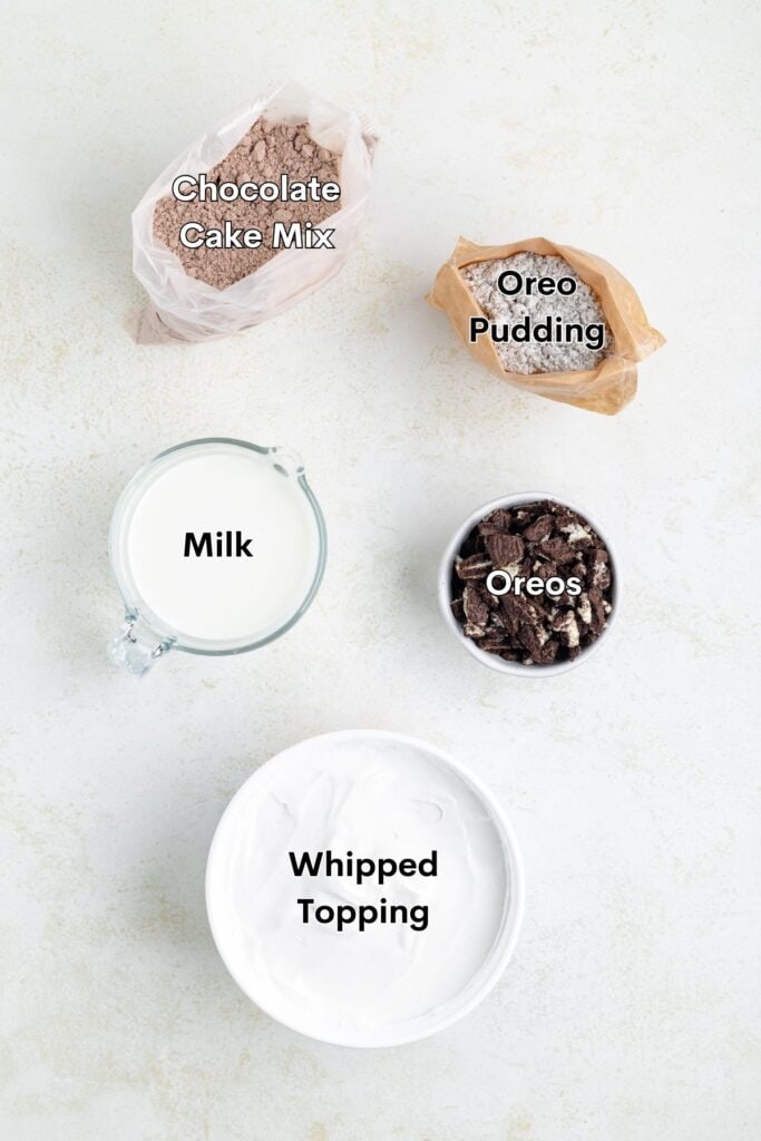 Ingredients for a dessert recipe are laid out: chocolate cake mix, Oreo pudding, milk, crushed Oreos, and whipped topping on a white surface.