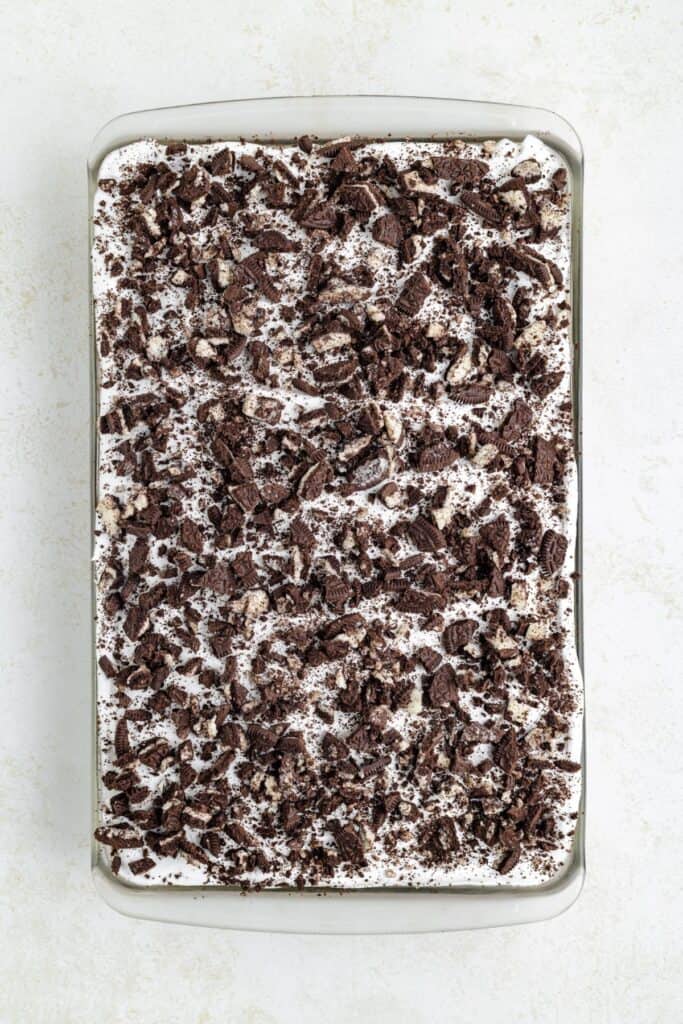 A rectangular cake topped with crushed chocolate cookies on a white surface.