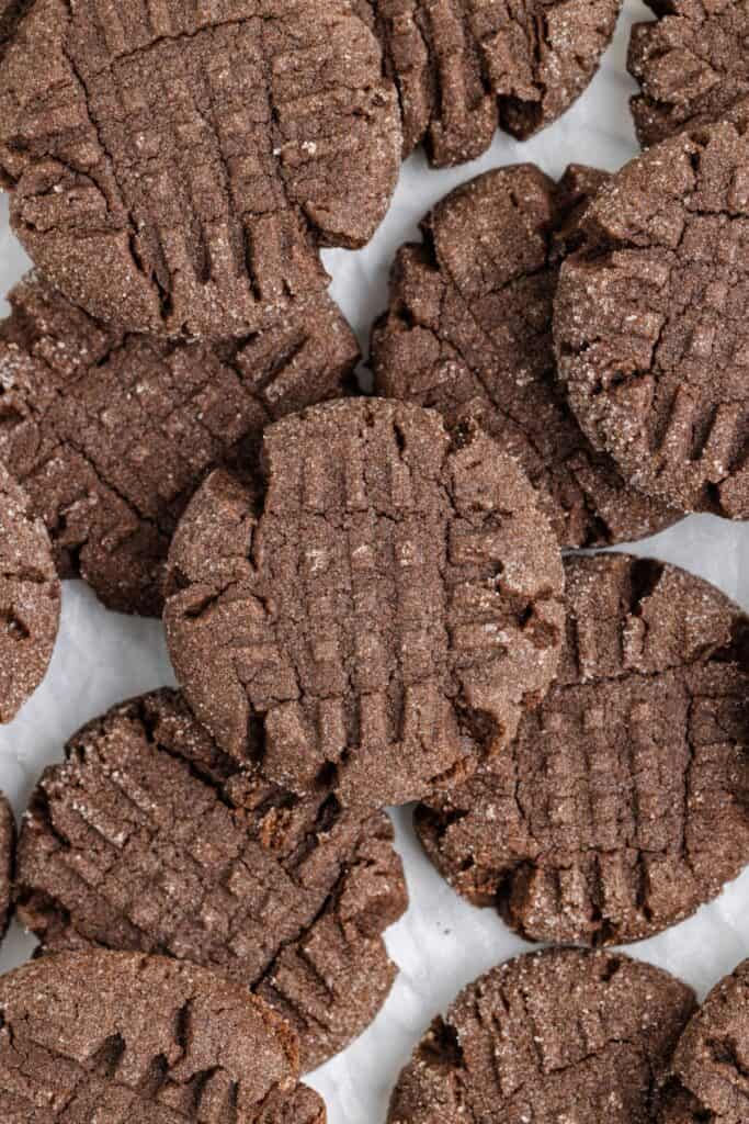 A close-up of a pile of peanut butter chocolate cake mix cookies with a crisscross pattern on top. The cookies are covered with a light dusting of sugar.