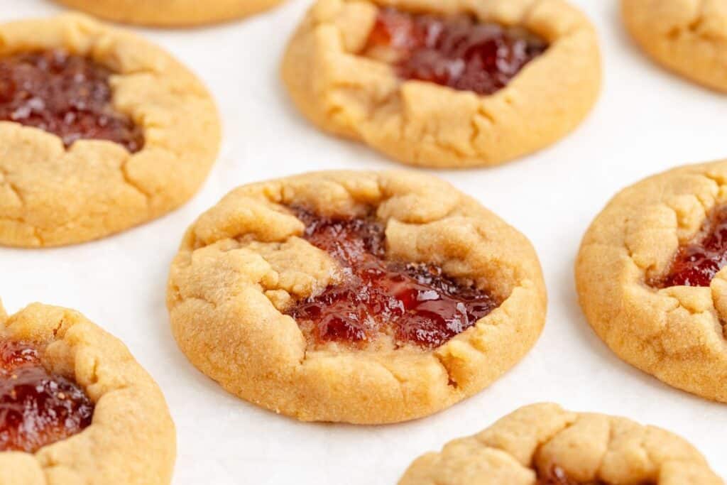 Jam-filled peanut butter cookies arranged on a white surface.