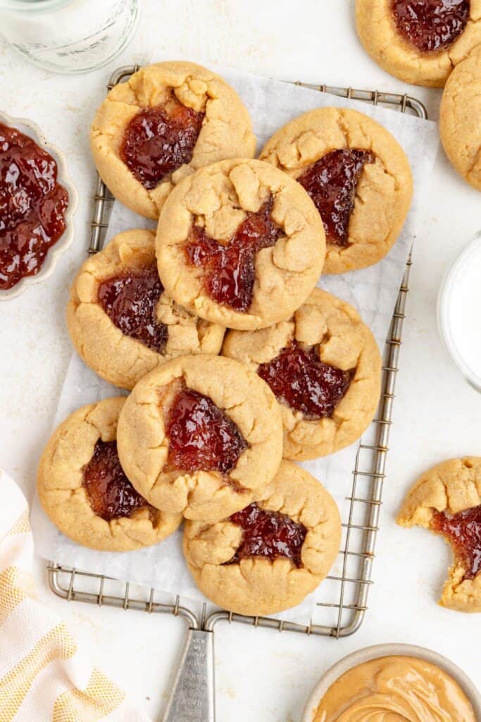 Peanut butter and jelly cookies on a cooling rack with peanut butter and jelly jars nearby.