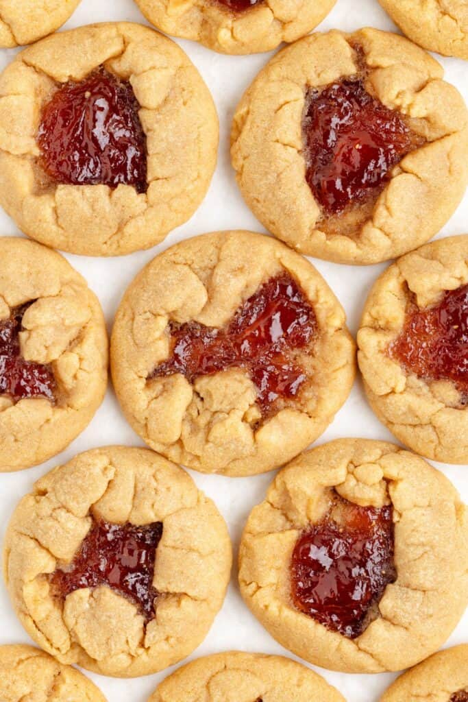 Close-up of peanut butter cookies with a dollop of red jelly in the center, arranged in rows.