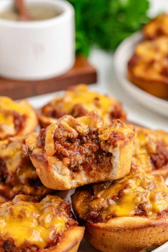 Close-up of Sloppy Joe biscuit cups topped with melted cheese and ground meat. One is partially eaten, revealing its savory filling. 