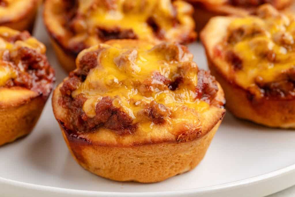 Individual Sloppy Joe Cups topped with melted cheese rest on a white plate.