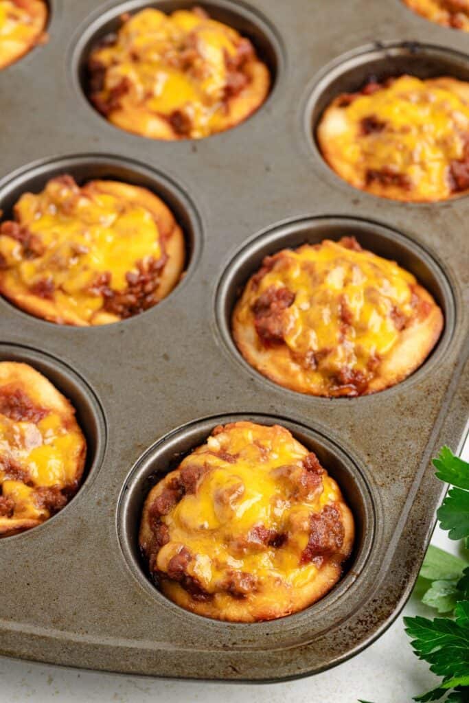 Muffin tin with baked sloppy joe cups topped with melted cheese.