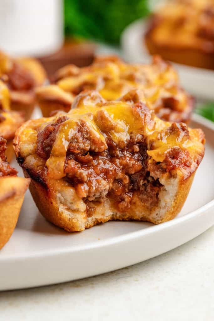 Close-up of a meaty Sloppy Joe Cup topped with melted cheese on a white plate, with a bite taken out of it, revealing the savory beef filling.