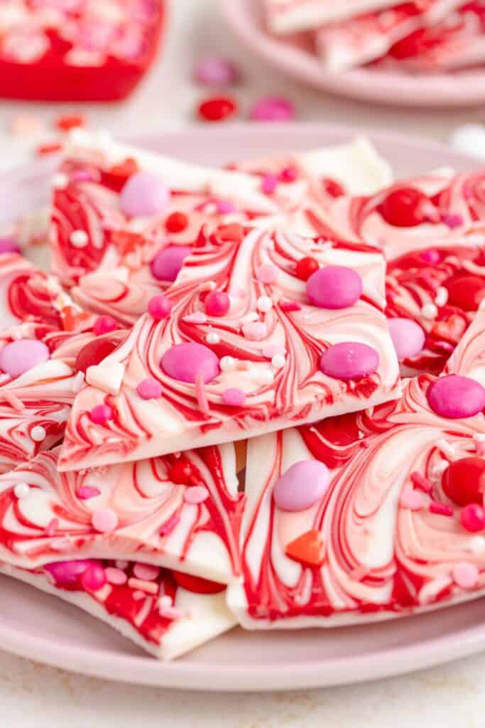 Pieces of Valentines Day Bark, featuring red and white swirled chocolate with pink and red sprinkles, sitting on a pink plate.