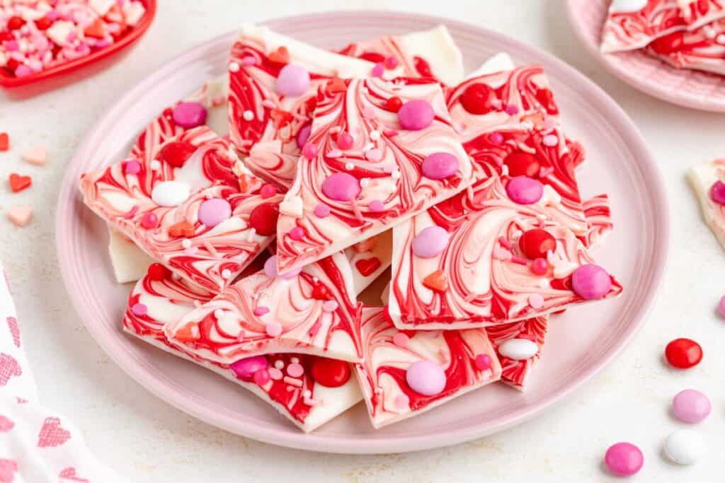 A plate of marbled pink, red, and white chocolate bark, topped with red, pink, and white candy pieces.