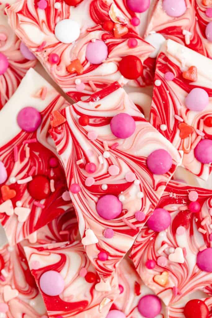 Close-up of pieces of pink and red swirled Valentine's Day chocolate bark topped with various colored candies and sprinkles.