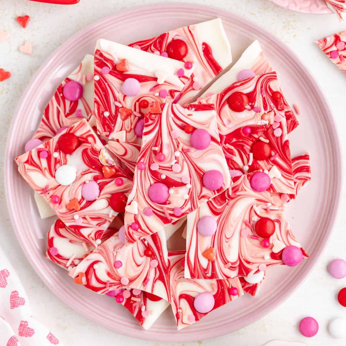 A plate of swirled white and red chocolate Valentines Day bark adorned with pink and red candy pieces.