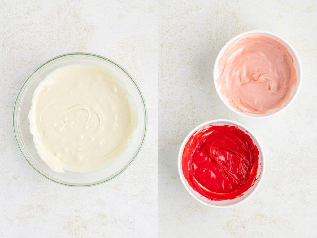 Three bowls of melted chocolate: one with white, one with pink, and one with red, placed on a light surface.