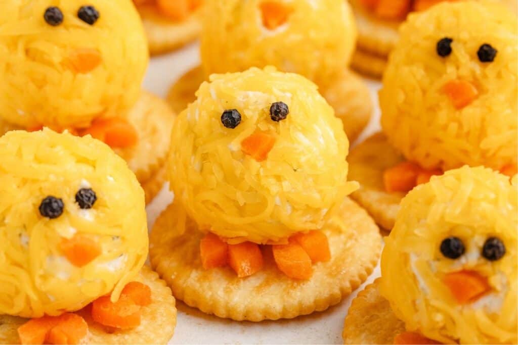 Playful appetizer baby chick cheese balls with carrot features on crackers.