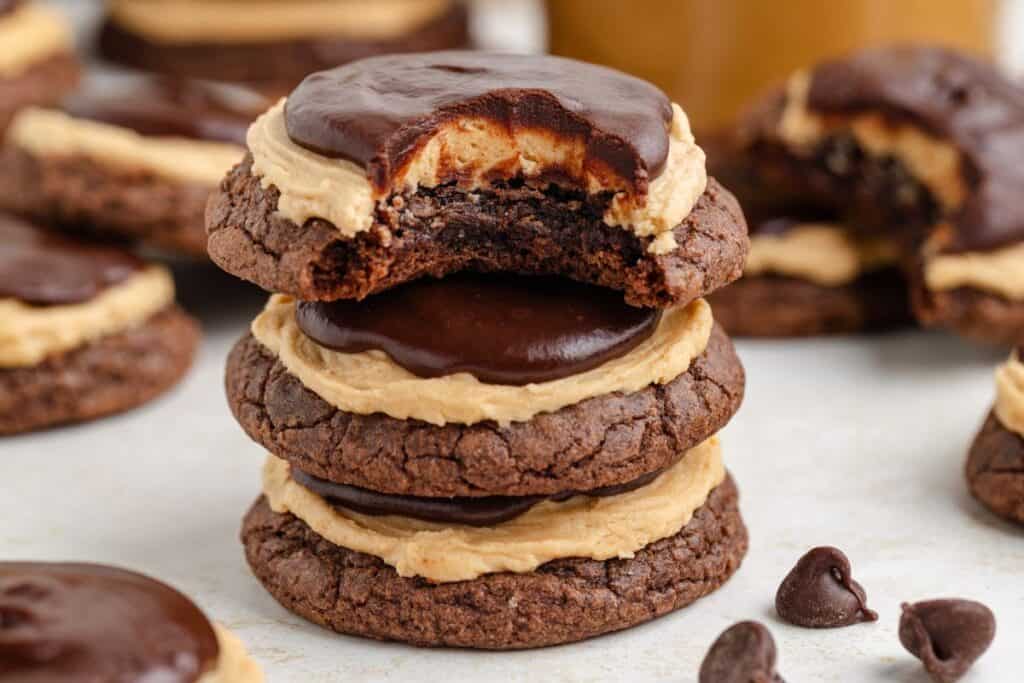 A stack of chocolate buckeye brownie cookies topped with peanut butter frosting and chocolate ganache, with a bite taken out of the top cookie.