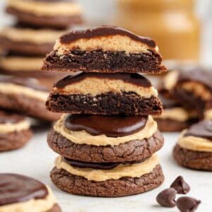 Close-up of stacked chocolate cookies with peanut butter filling, topped with chocolate frosting. Other cookies are arranged in the background.