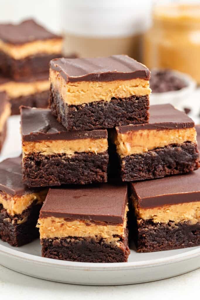 A stack of chocolate peanut butter brownies with chocolate ganache topping on a white plate. 