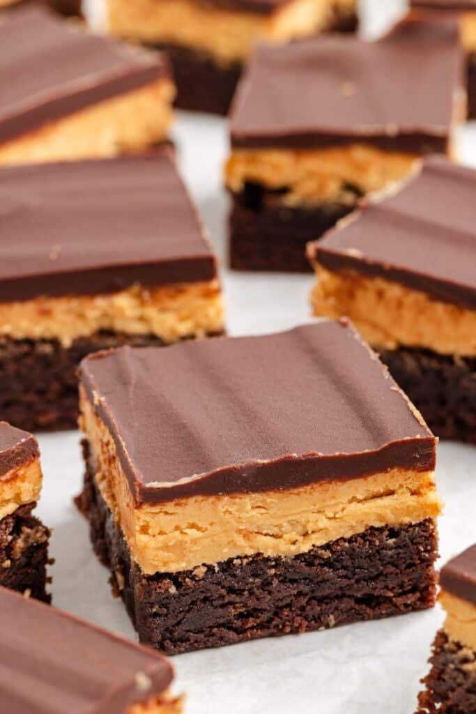 Close-up of layered chocolate peanut butter brownies with a thick chocolate topping, arranged on a white surface.