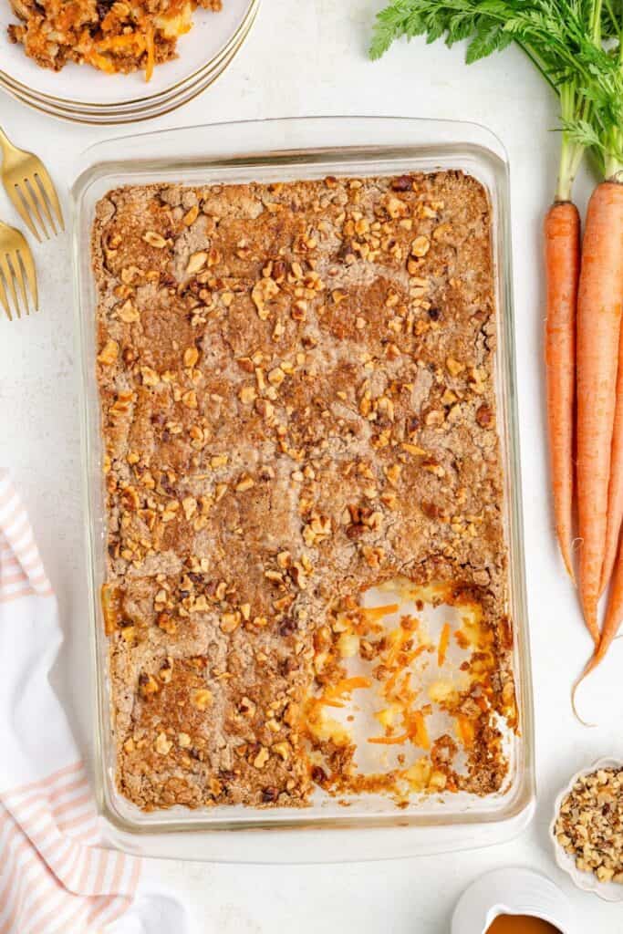 Glass baking dish with a square piece removed, filled with carrot dump cake topped with walnuts.