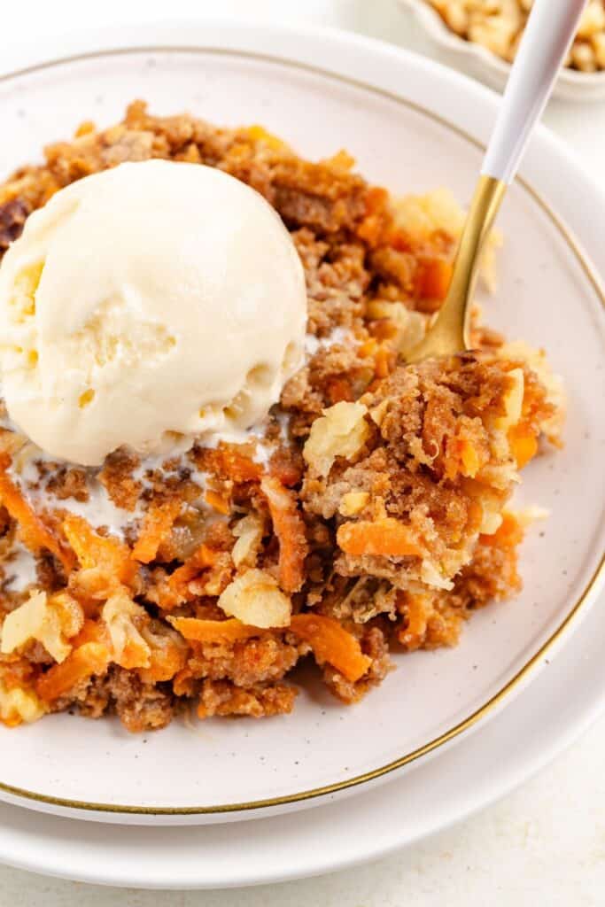 A plate of carrot  dump cake topped with a scoop of vanilla ice cream, with a fork holding a bite.