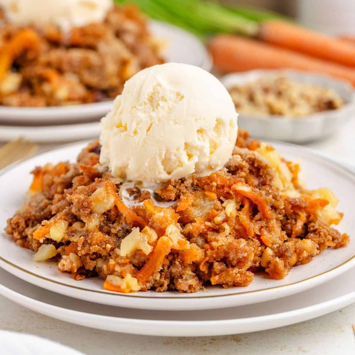 A plate of carrot dump cake topped with a scoop of vanilla ice cream. Carrots and chopped walnuts are visible in the background.